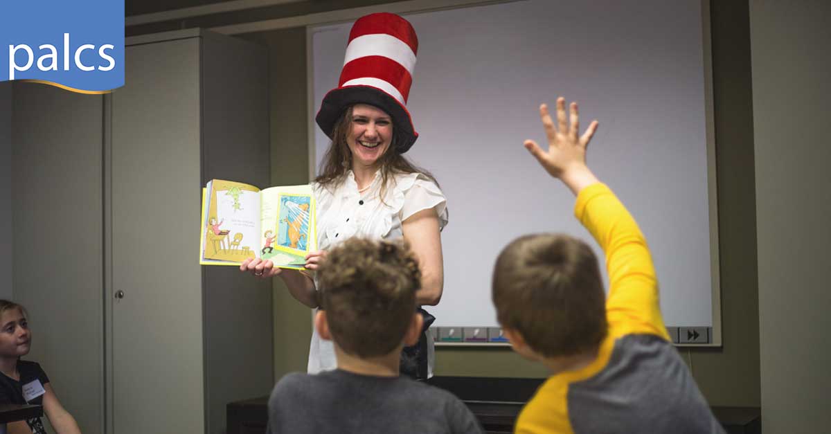 student raising hand while ms. owens reads a book